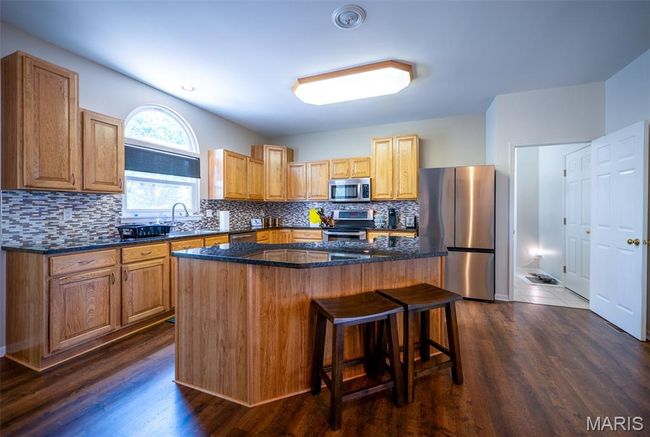 Kitchen with appliances with stainless steel finishes, a breakfast bar area, tasteful backsplash, a kitchen island, and dark stone countertops | Image 8