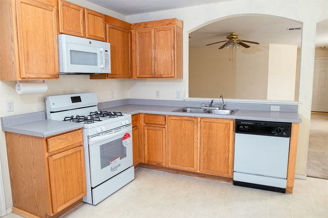 Kitchen featuring white appliances, a sink, ceiling fan, light countertops, and arched walkways | Image 11
