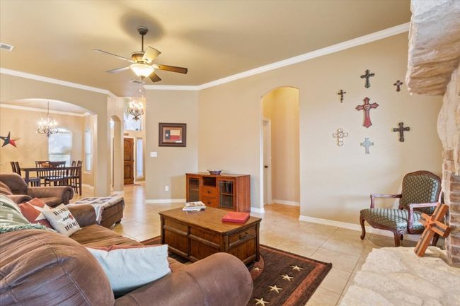 Living room featuring light tile patterned floors, visible vents, arched walkways, ornamental molding, and ceiling fan with notable chandelier | Image 10