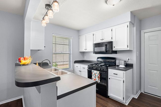 Kitchen featuring black appliances, white cabinets, a sink, dark wood finished floors, and dark countertops | Image 9