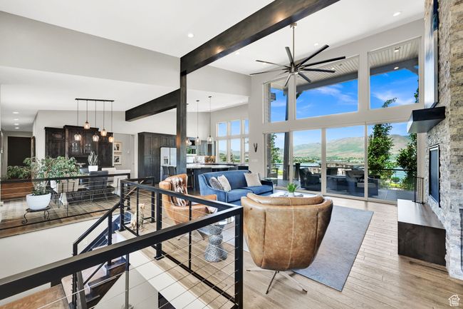 Living room lake view featuring a fireplace, beamed ceiling, a high ceiling, ceiling fan, and light wood-style flooring | Image 13