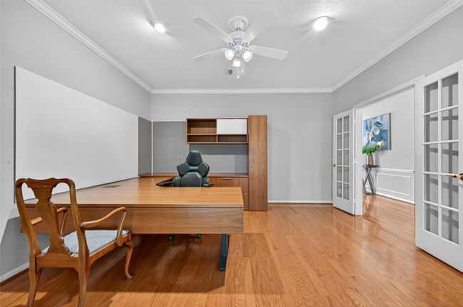 This photo showcases a spacious home office with hardwood floors, a ceiling fan, and modern furniture. It features French doors and a neutral color palette, creating a bright and welcoming workspace. | Image 34