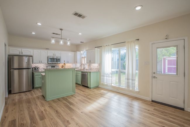 Kitchen featuring stainless steel appliances, visible vents, light wood-type flooring, green cabinets, and a center island | Image 7