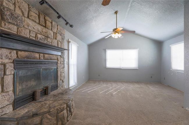 Unfurnished living room with a textured ceiling, vaulted ceiling, a ceiling fan, and a wealth of natural light | Image 16