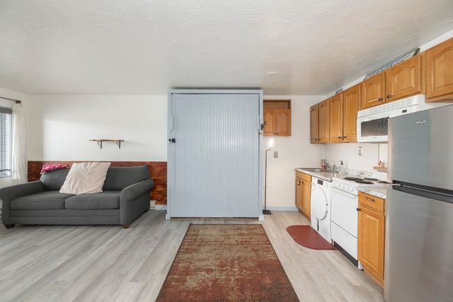 Kitchen featuring white appliances, open floor plan, light wood-style floors, washer / dryer, and brown cabinets | Image 4