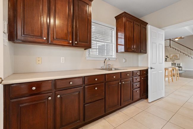 Laundry/Utility room showing ample counter top space, full size bay sink, built in ironing board, upper/lower cabinets for storage. Washer/dryer space is to the right of this photo with an additional closet beside that. Full bath to the left as you enter from the kitchen door you see. Door to the left (you cna barely see the door knob) is the entrance from the porte-cochere. | Image 34