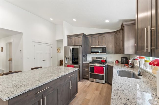 Kitchen featuring stainless steel appliances, a sink, vaulted ceiling, dark brown cabinets, and light stone countertops | Image 8