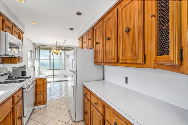 Kitchen featuring light tile patterned flooring, white appliances, brown cabinetry, and a chandelier | Image 4