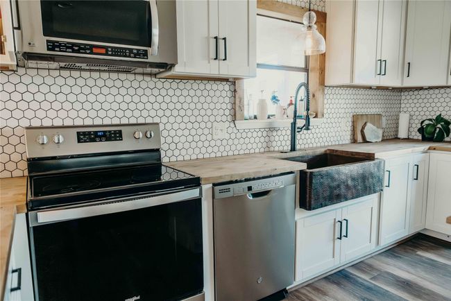 Kitchen featuring stainless steel appliances, wood counters, decorative backsplash, and white cabinetry | Image 13