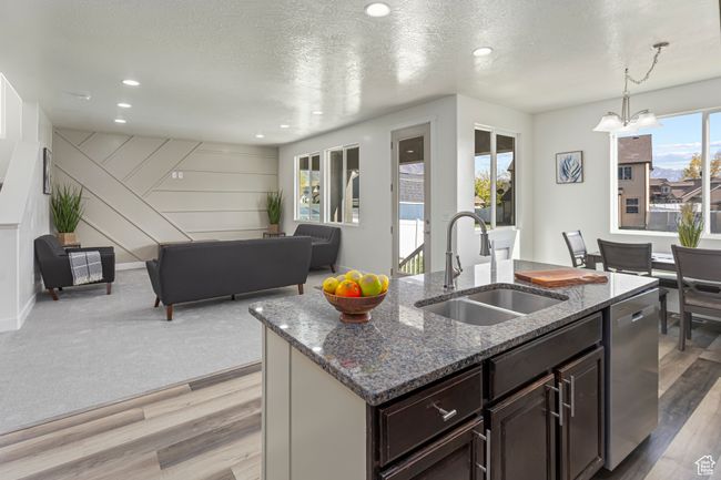 Kitchen with dark stone countertops, stainless steel dishwasher, a center island with sink, and a sink | Image 6