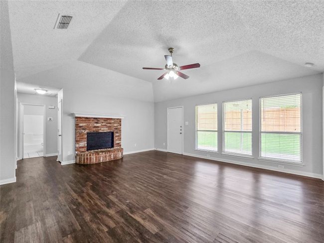 Unfurnished living room with dark wood-style flooring, healthy amount of natural light, a ceiling fan, a textured ceiling, and lofted ceiling | Image 13