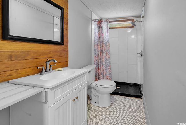 Bathroom featuring toilet, vanity, curtained shower, tile patterned flooring, and wood walls | Image 23