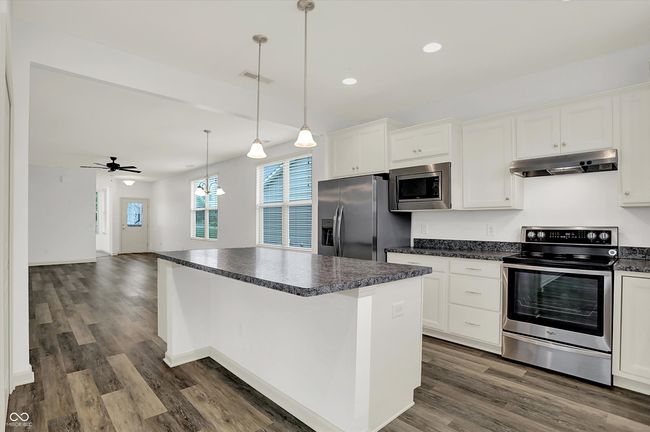 kitchen featuring stainless steel appliances, under cabinet range hood, dark countertops, a center island, and dark wood-type flooring | Image 9