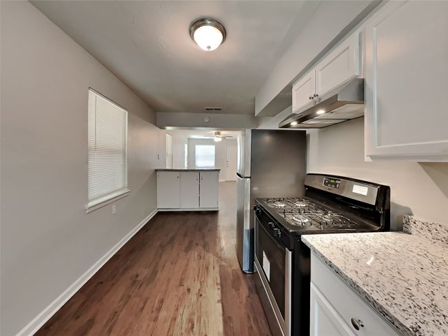 Kitchen with appliances with stainless steel finishes, under cabinet range hood, dark wood-style floors, white cabinets, and a ceiling fan | Image 5