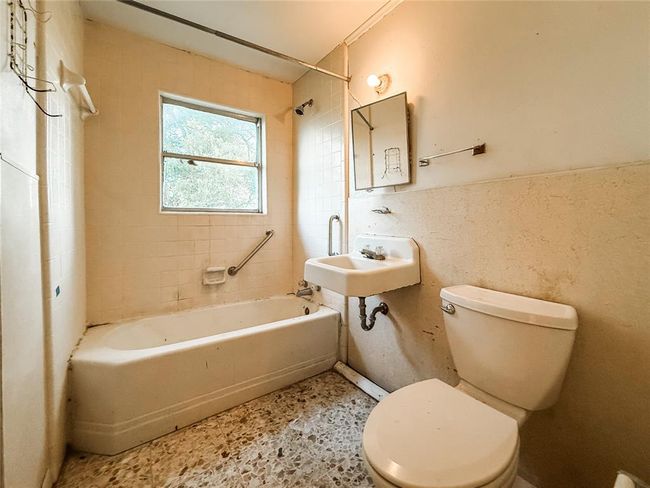 This bathroom features a vintage setup with a cast iron bathtub, toilet, and sink. It has a window for natural light and requires some updates for modernization. | Image 12