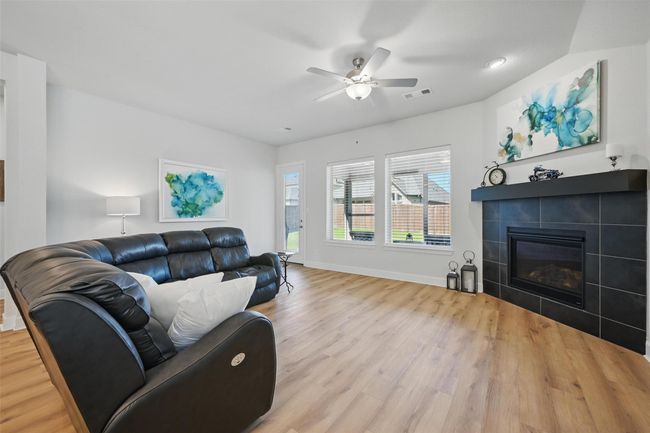 Living room featuring wood finished floors, a ceiling fan, a tile fireplace, and baseboards | Image 7