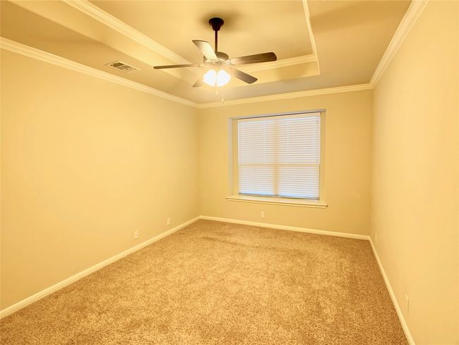 Carpeted empty room featuring a raised ceiling, ceiling fan, ornamental molding, and baseboards | Image 19