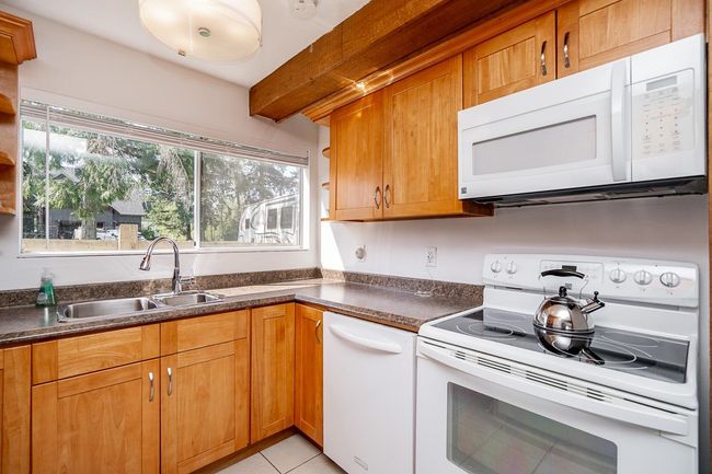 Kitchen featuring white appliances, open shelves, dark countertops, a sink, and beam ceiling | Image 34