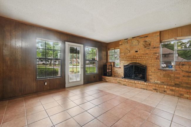 Unfurnished living room featuring healthy amount of natural light, a textured ceiling, a fireplace, wooden walls, and light tile patterned flooring | Image 10