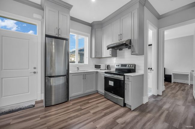 Kitchen featuring stainless steel appliances, under cabinet range hood, ornamental molding, wood finished floors, and light countertops | Image 23