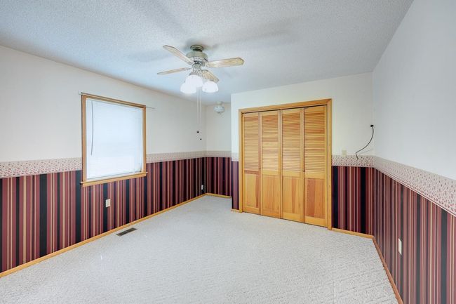 Unfurnished bedroom with a wainscoted wall, a closet, carpet, a textured ceiling, and a ceiling fan | Image 12