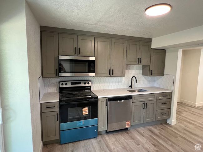 Kitchen featuring appliances with stainless steel finishes, gray cabinetry, tasteful backsplash, light wood-style floors, and a textured ceiling | Image 13