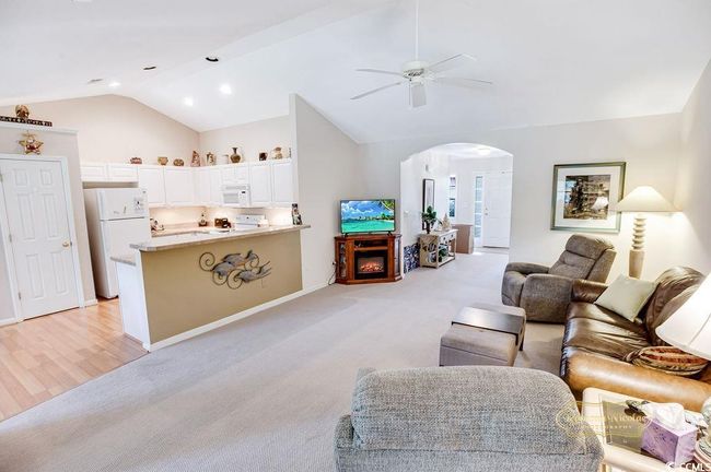 Living room with arched walkways, a ceiling fan, lofted ceiling, light colored carpet, and a lit fireplace | Image 12