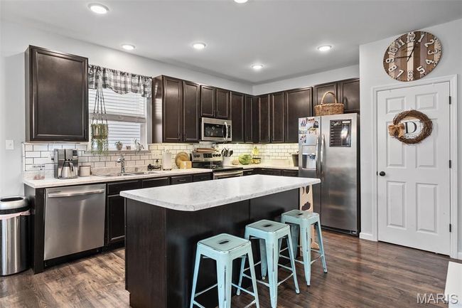 Kitchen with stainless steel appliances, a breakfast bar area, light countertops, dark wood-style floors, and recessed lighting | Image 10