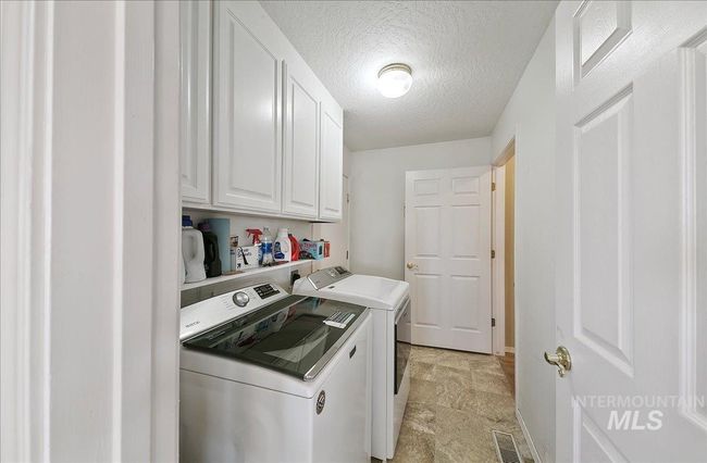 Laundry area featuring washer and dryer, cabinet space, a textured ceiling, and light stone finish flooring | Image 35