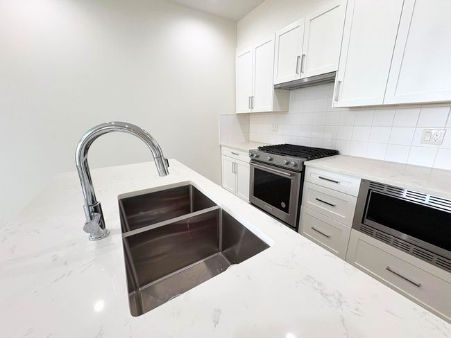 Kitchen featuring stainless steel appliances, decorative backsplash, light stone counters, white cabinetry, and under cabinet range hood | Image 5