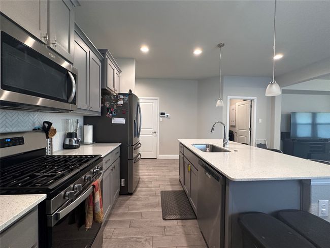 Kitchen featuring stainless steel appliances, light wood-style floors, gray cabinetry, a kitchen island with sink, and recessed lighting | Image 7