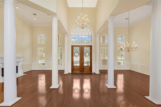 The grand open foyer with high ceilings, elegant chandeliers, and large windows with shutter that let in plenty of natural light. The space features polished hardwood floors, decorative columns, and a classic fireplace, creating a luxurious and welcoming entryway. | Image 7