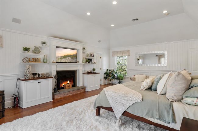 Bedroom featuring visible vents, wood finished floors, vaulted ceiling, and a glass covered fireplace | Image 32
