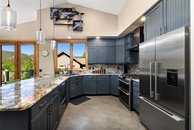 Kitchen featuring stainless steel appliances, wall chimney range hood, light stone counters, a peninsula, and high vaulted ceiling | Image 4