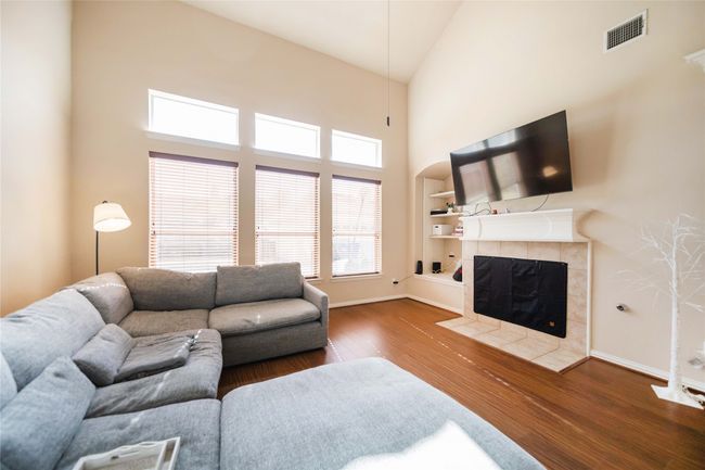 Living room with wood finished floors, a fireplace, and a high ceiling | Image 18