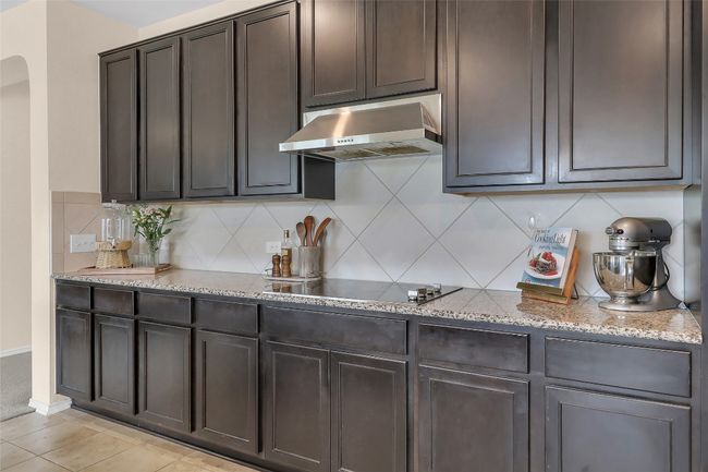 Kitchen with exhaust hood, black electric stovetop, light stone counters, decorative backsplash, and arched walkways | Image 10