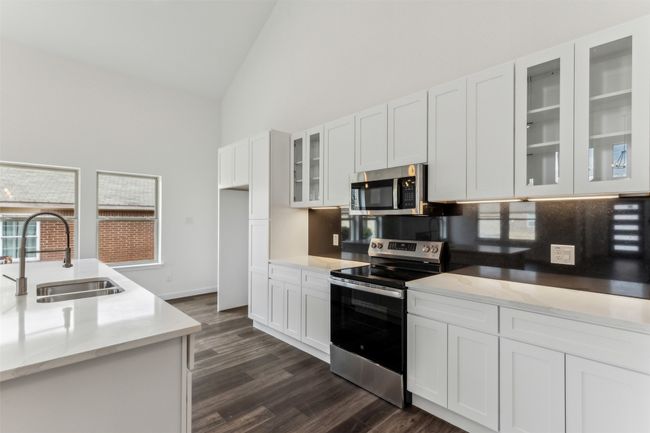 Kitchen featuring stainless steel appliances, high vaulted ceiling, dark wood-style flooring, white cabinets, and glass insert cabinets | Image 21