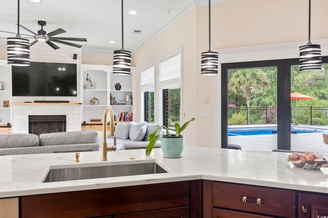 Kitchen featuring a sink, open floor plan, ceiling fan, light stone counters, and crown molding | Image 12