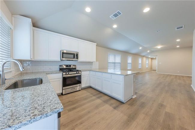 Kitchen featuring stainless steel appliances, a sink, vaulted ceiling, decorative backsplash, and white cabinets | Image 8