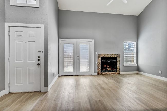 Unfurnished living room featuring wood finished floors, baseboards, ceiling fan, a towering ceiling, and a fireplace | Image 6