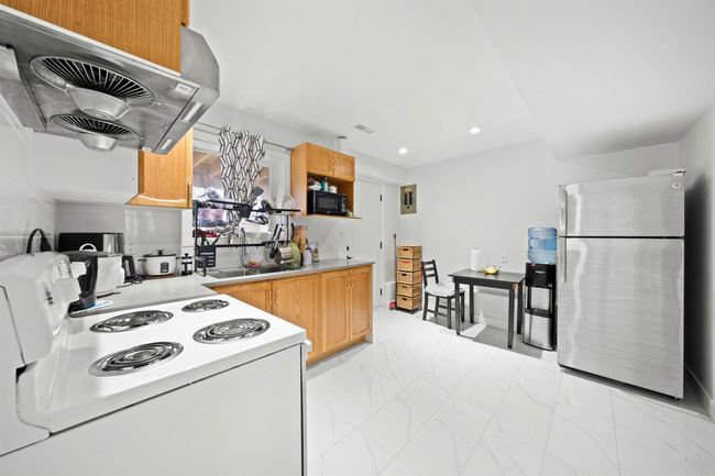 Kitchen with freestanding refrigerator, black microwave, white range with electric stovetop, exhaust hood, and marble finish floor | Image 18
