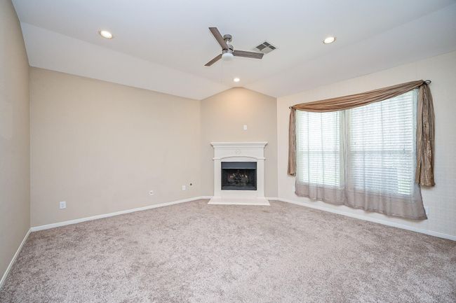 Bright living room with carpeted flooring and large window. Recessed lighting and a ceiling fan enhance the modern feel. | Image 15