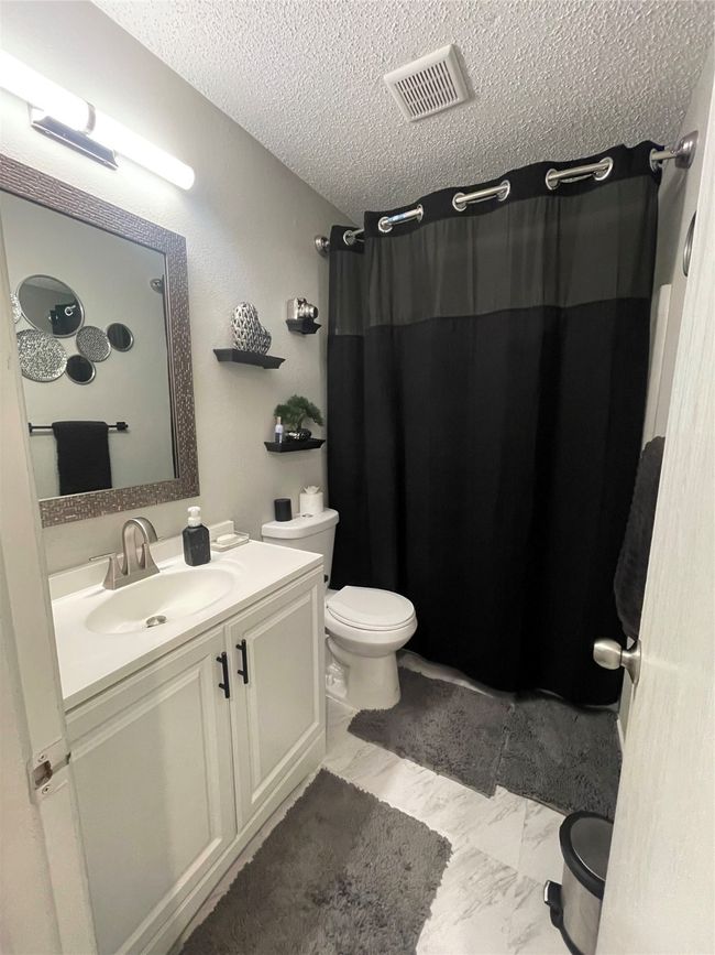 Full bathroom featuring a textured ceiling, vanity, a shower with shower curtain, and marble look tiles | Image 18