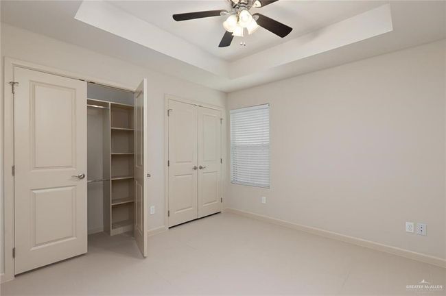 Unfurnished bedroom with two closets, a tray ceiling, and a ceiling fan | Image 12