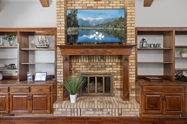 Striking focal wall in the main-floor family room featuring a brick-front gas fireplace, soaring vaulted ceilings, Mahogany cabinets and shelves, and abundant natural light streaming through a picturesque window. | Image 17