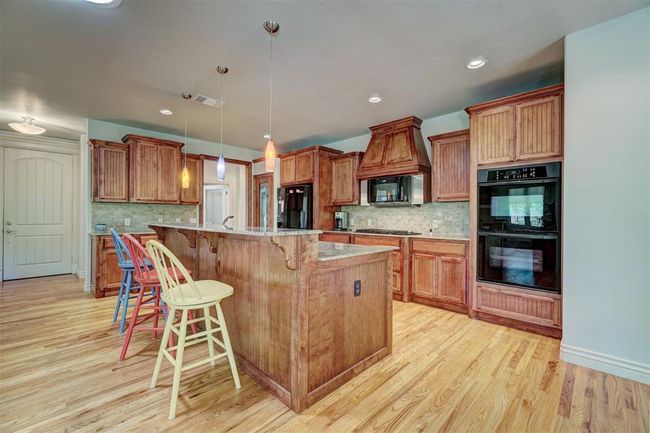 Kitchen featuring a kitchen breakfast bar, tasteful backsplash, light wood-type flooring, brown cabinets, and black appliances | Image 12