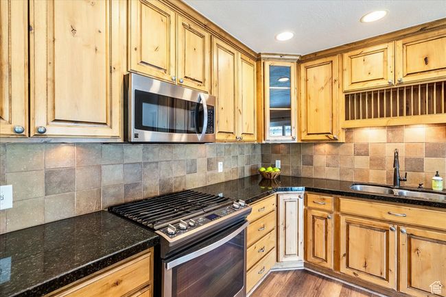 Kitchen with appliances with stainless steel finishes, dark stone counters, backsplash, light wood finished floors, and glass insert cabinets | Image 20