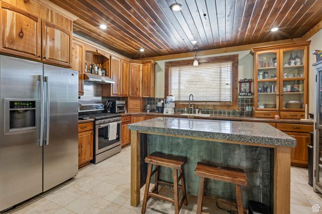 Kitchen with appliances with stainless steel finishes, a sink, wooden ceiling, a breakfast bar area, and open shelves | Image 9