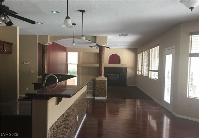 Kitchen featuring a ceiling fan, dark wood finished floors, a glass covered fireplace, healthy amount of natural light, and a textured ceiling | Image 6
