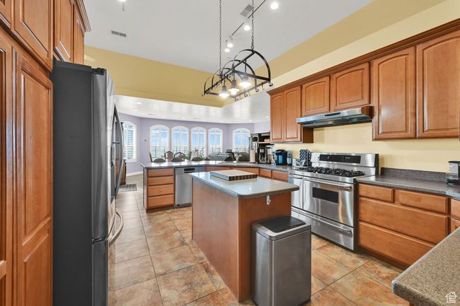Kitchen featuring a peninsula, a sink, under cabinet range hood, appliances with stainless steel finishes, and a kitchen island | Image 19